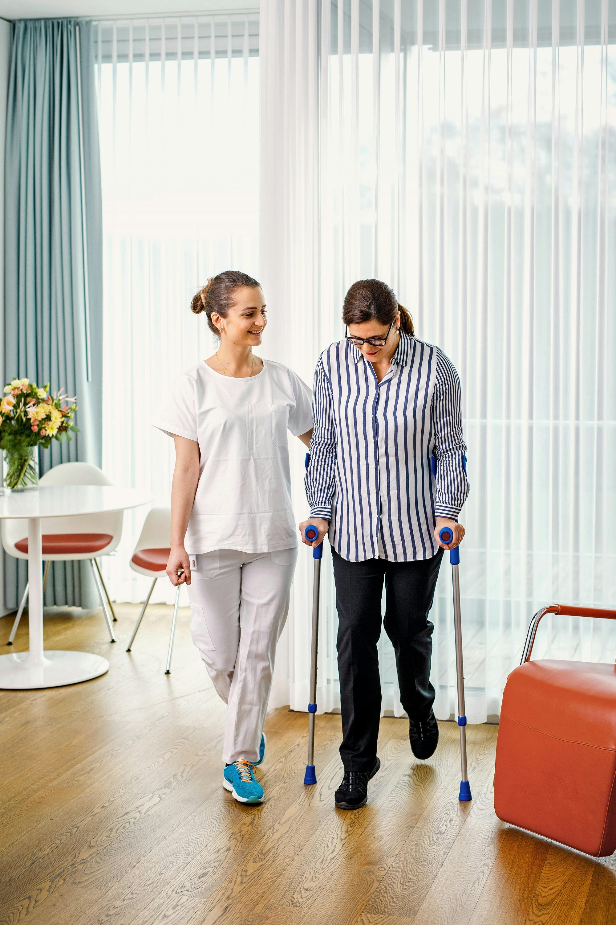 Physiotherapist supports a patient with walking aids during rehabilitation in a bright clinic.