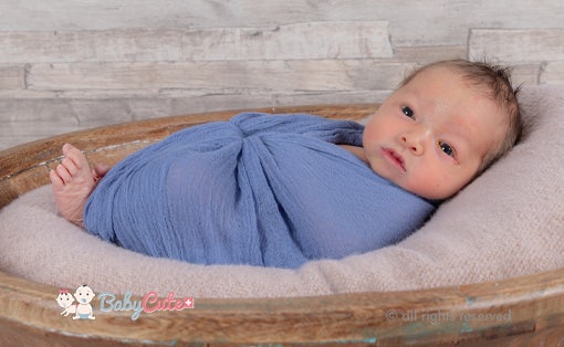 Neugeborenes eingewickelt in blaue Decke auf Korb, Holzhintergrund.