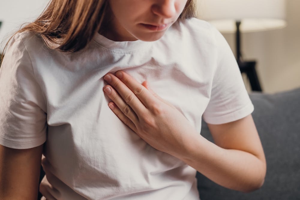 Woman in white T-shirt holds hand on chest, pain or discomfort gesture.