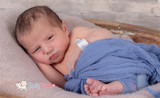 Neugeborenes eingewickelt in eine blaue Decke mit einem Schnuller neben sich.