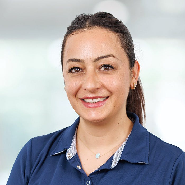Portrait of a smiling woman with a ponytail and polo shirt against a blurred background.