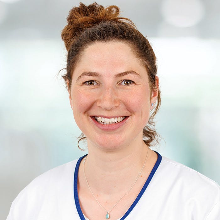 Smiling woman with a bun, in medical professional clothing.