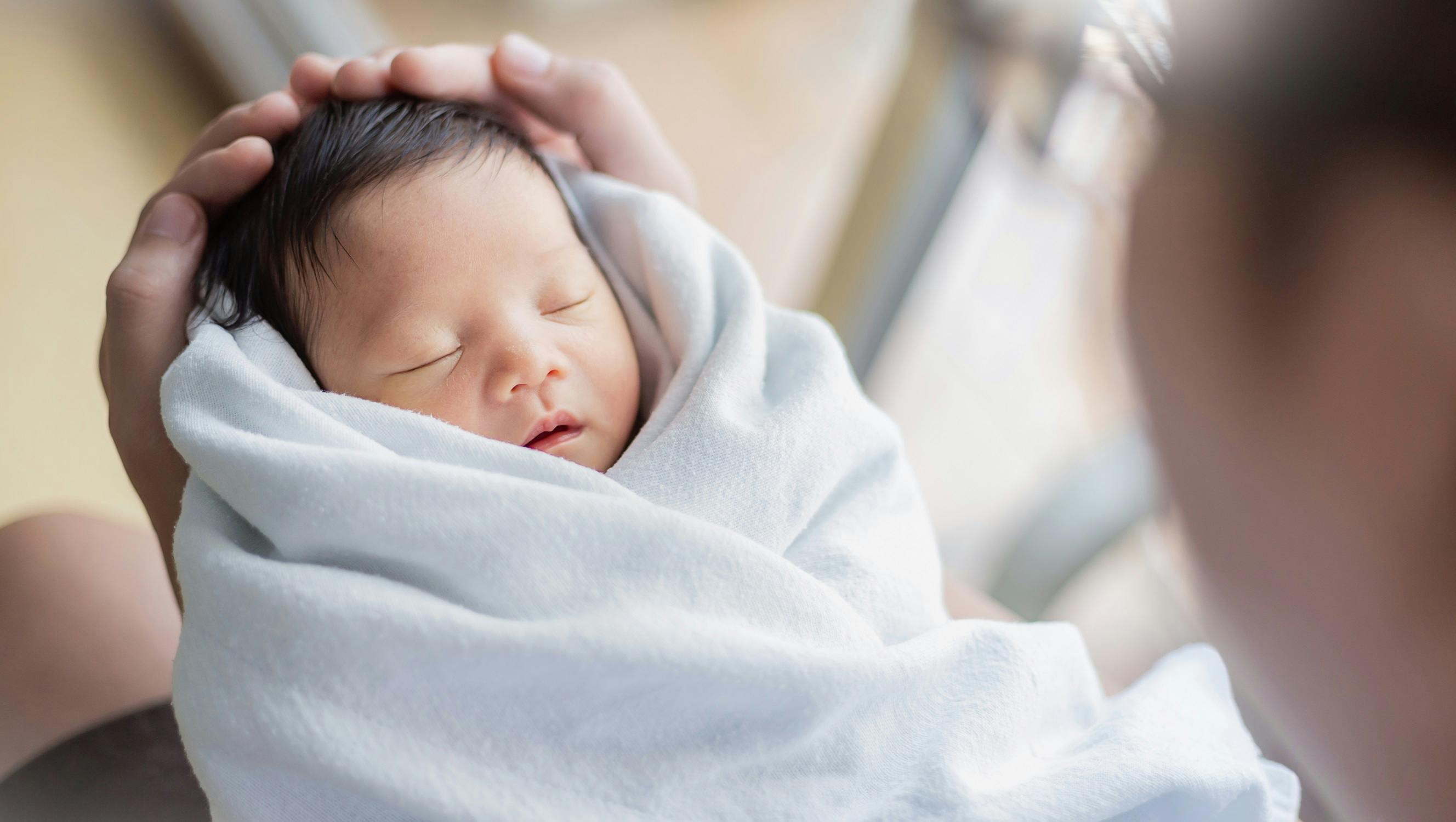 Neugeborenes schläft friedlich eingewickelt in eine weiße Decke.