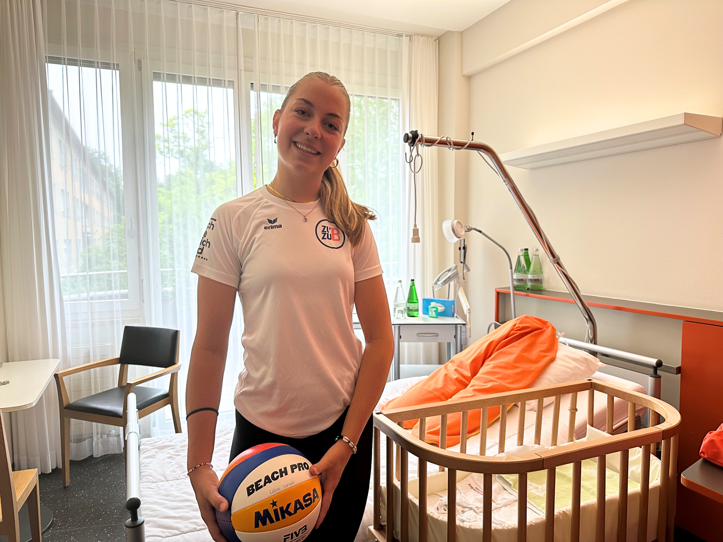 Woman in a hospital room holding a volleyball and wearing sportswear. 