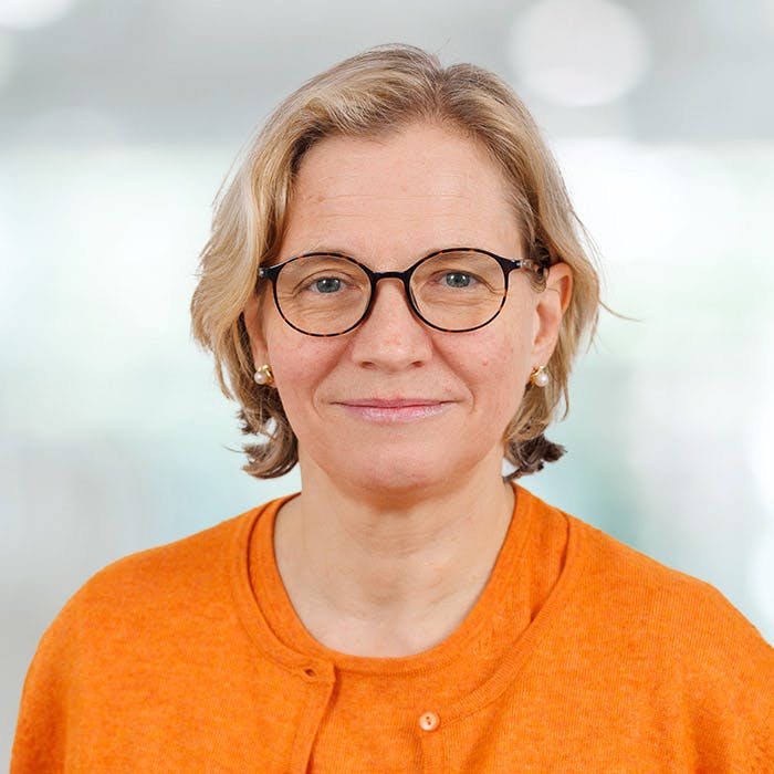 Portrait of a smiling woman with glasses and an orange top.