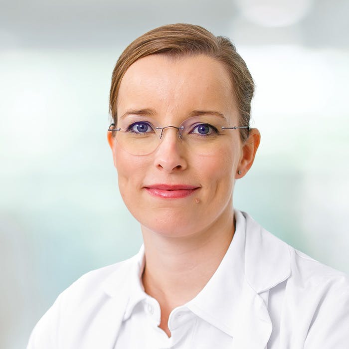 Portrait of a smiling woman with glasses and a white lab coat.