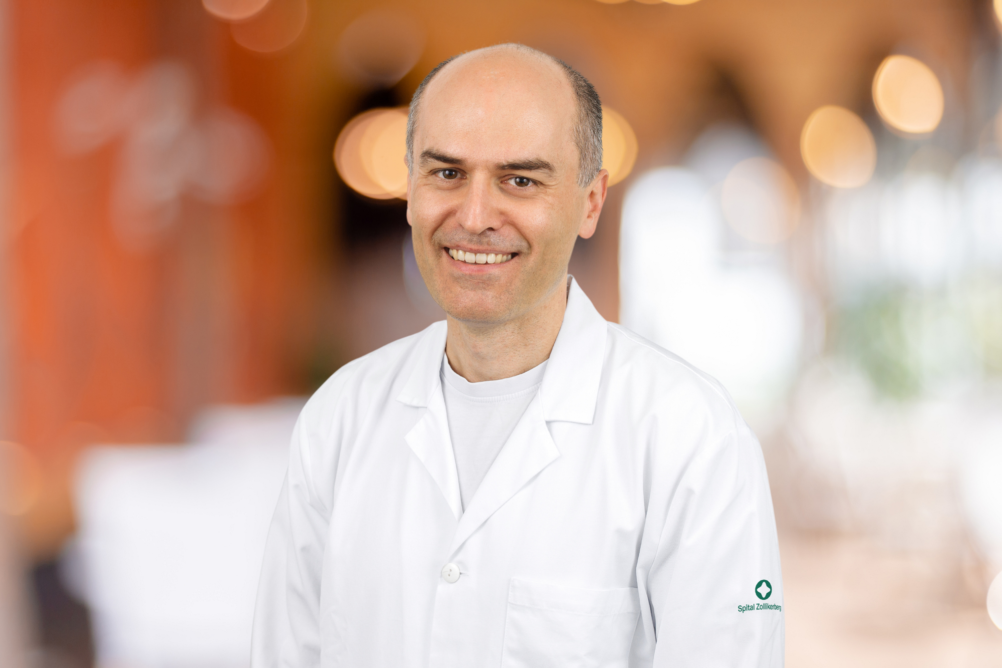 Smiling doctor in a white coat in front of a blurred background.