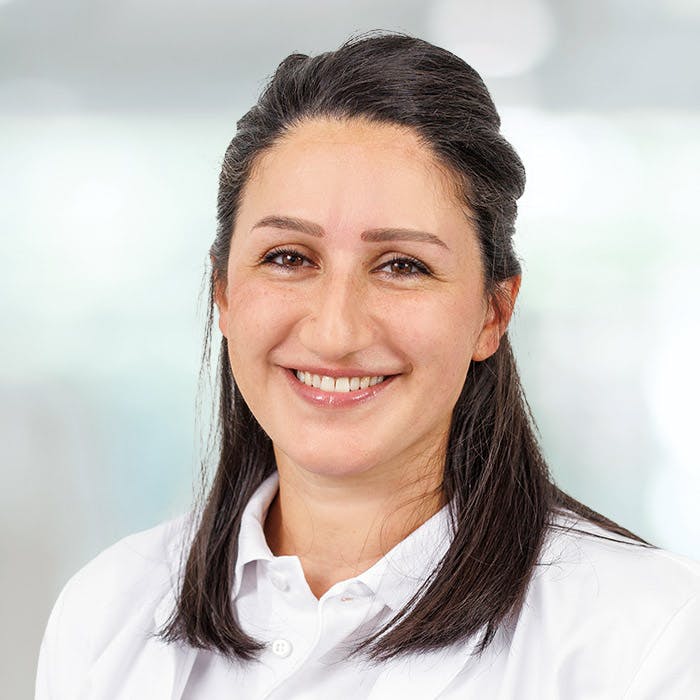 Portrait of a smiling woman with dark hair in a white shirt, blurred background.