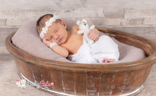 Neugeborenes schläft in einem Korb mit Kuscheltier und Haarband.