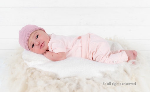 Newborn baby in pink clothes lying on a soft surface.