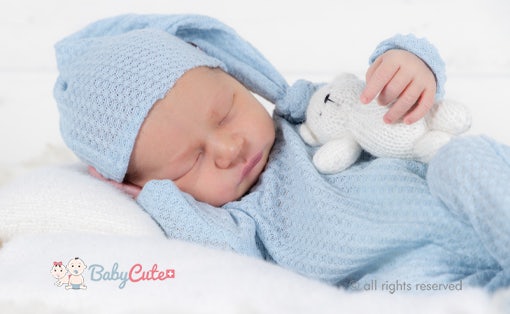 Schlafendes Baby in blauer Strickmütze und Decke mit Kuscheltier.