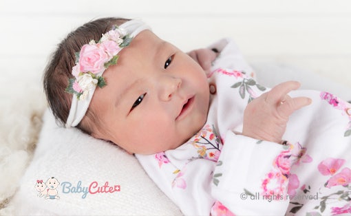 Niedliches Baby mit Blumenhaarband lächelt in die Kamera.