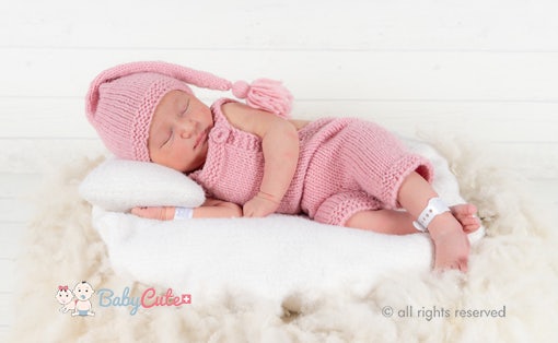Neugeborenes schläft in rosa Strickkleidung auf weißer Decke.