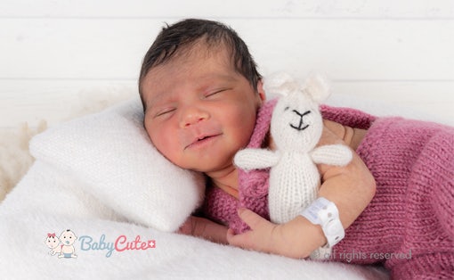 Neugeborenes mit geschlossenen Augen hält ein Stofftier, umgeben von weichen Decken.