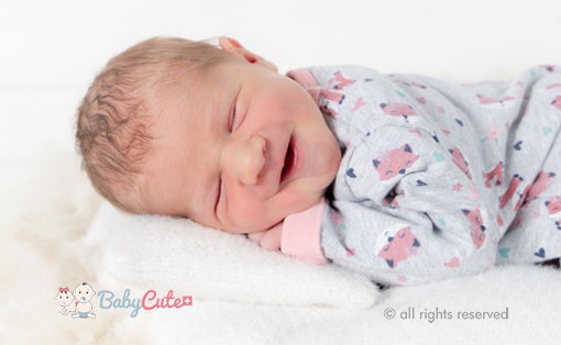 Neugeborenes Baby lacht im Schlaf, eingewickelt in eine Decke mit niedlichem Muster.