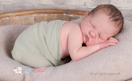 Neugeborenes schläft eingewickelt in grünes Tuch.