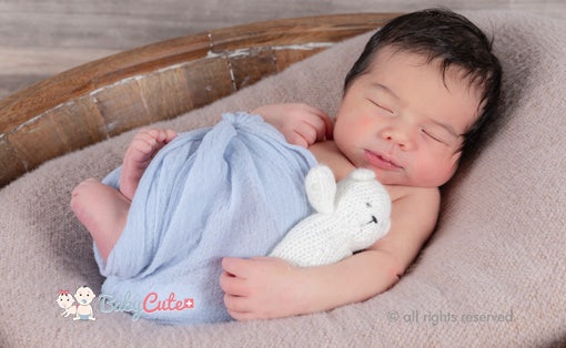 Neugeborenes schläft in Holzschale mit blauer Decke und weißem Spielzeughasen.