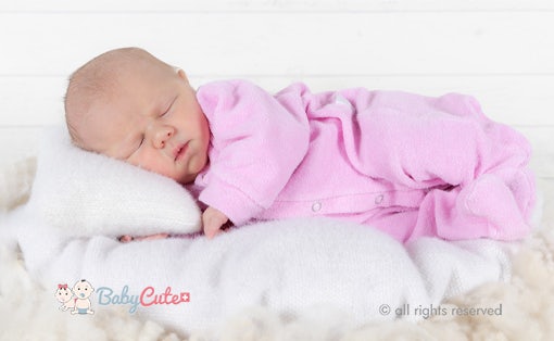 Schlafendes Neugeborenes in rosa Strampler liegt auf weißer Decke.