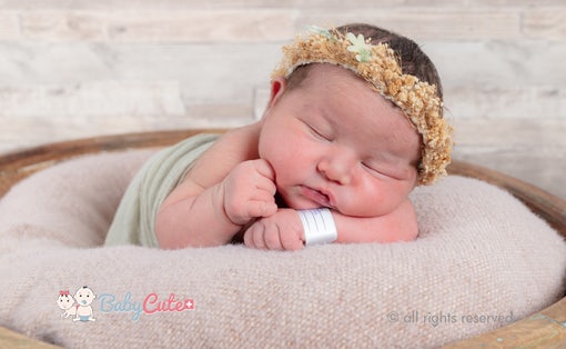 Newborn baby sleeping with a flower crown on a soft surface.