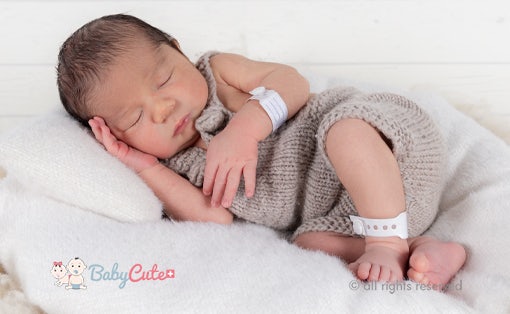 Schlafendes Neugeborenes in Strickkleidung auf weißer Decke.