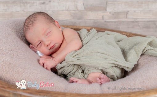 Neugeborenes schläft in einer Korbwiege, bedeckt mit einem grünen Tuch.