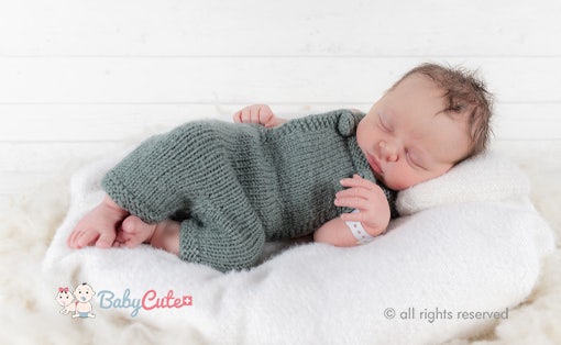 Sleeping newborn baby in green knitted clothes on a white blanket.