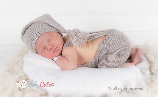 Schlafendes Neugeborenes in gestricktem Outfit auf weißer Decke.