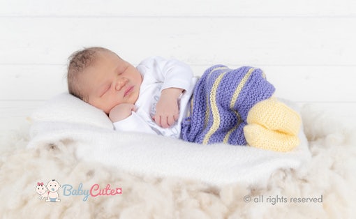 Schlafendes Neugeborenes mit gestrickter Decke auf weicher Unterlage.