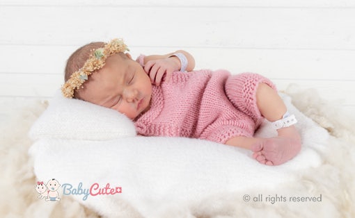 Neugeborenes in rosa Strickkleidung und Blumenhaarband schläft friedlich.