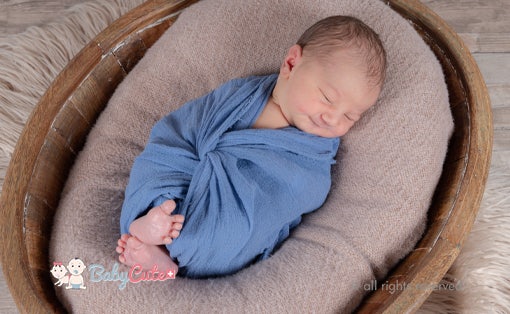 Neugeborenes eingewickelt in eine blaue Decke schläft friedlich.