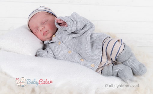 Schlafendes Baby in grauer Strickkleidung auf weißem Hintergrund.