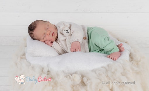 Schlafendes Neugeborenes eingewickelt in eine weiße Decke auf weicher Unterlage.