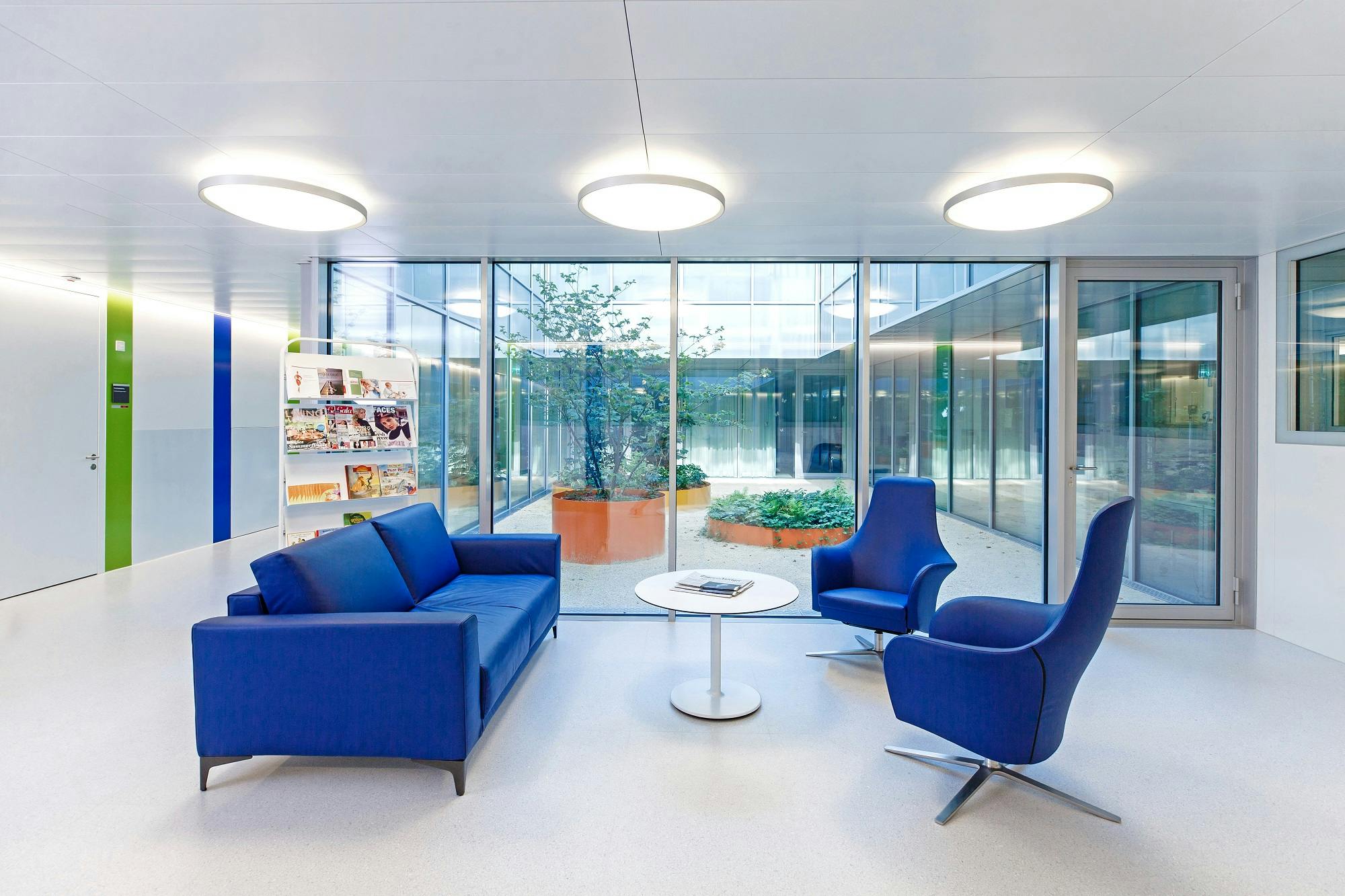 Modern waiting area with blue sofas, magazine rack and view of an inner courtyard.