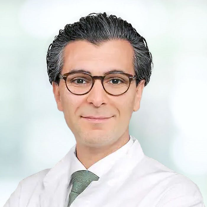 Portrait of a smiling male doctor with glasses and a green tie.