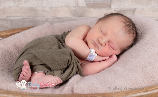 Schlafendes Neugeborenes in grünem Tuch auf rosa Decke.