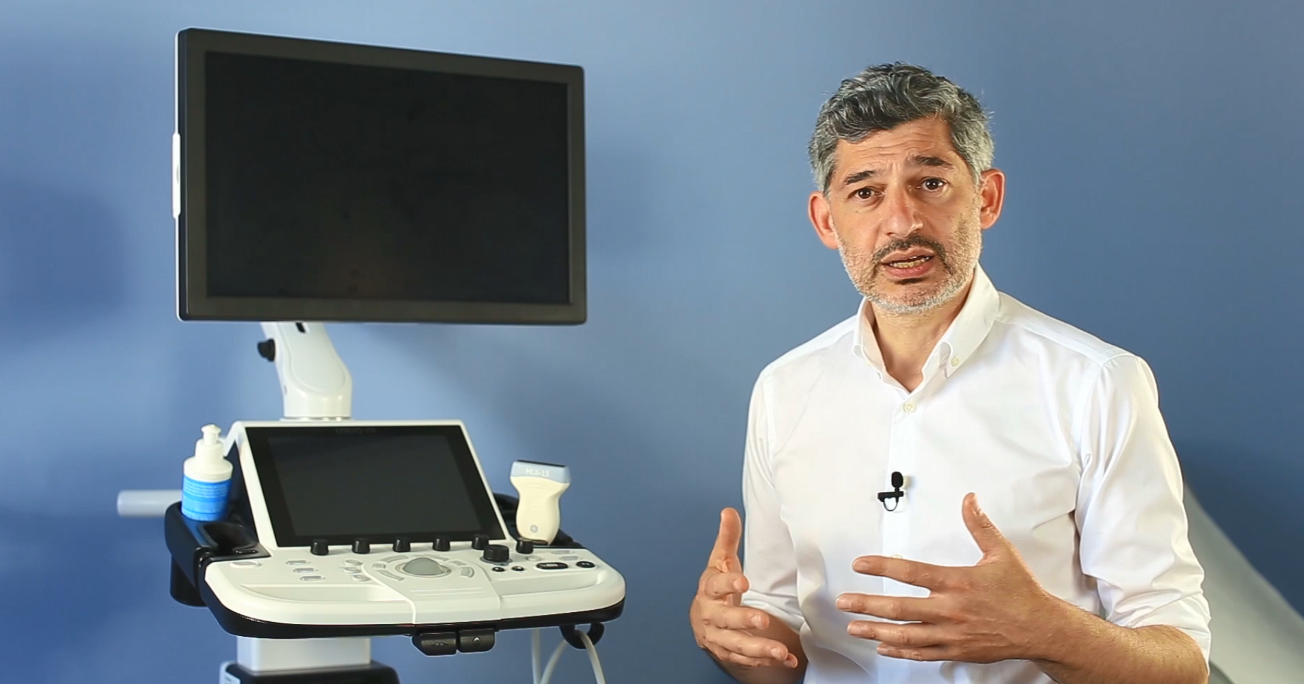 Mann in weißem Hemd vor Ultraschallgerät mit Monitor im Hintergrund.