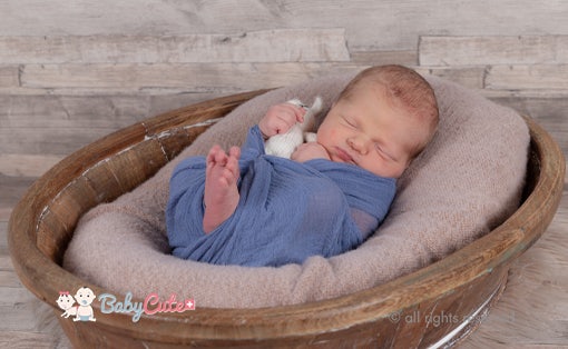 Newborn baby sleeping in a basket, wrapped in a blue blanket.