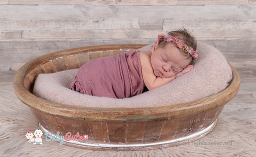 Neugeborenes schläft in einem Korb, umwickelt in ein rosa Tuch und mit Blumenhaarkranz.