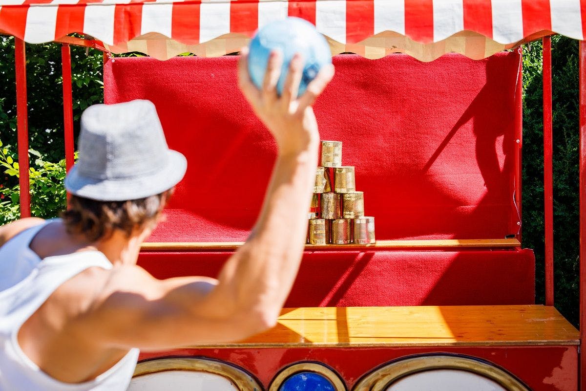 A person throws a ball at a pyramid of cans at a fairground game.
