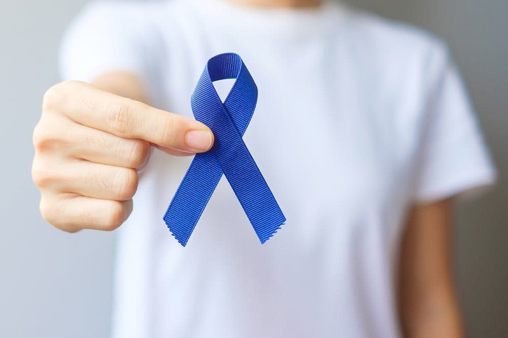 Person holds blue awareness ribbon in hand.