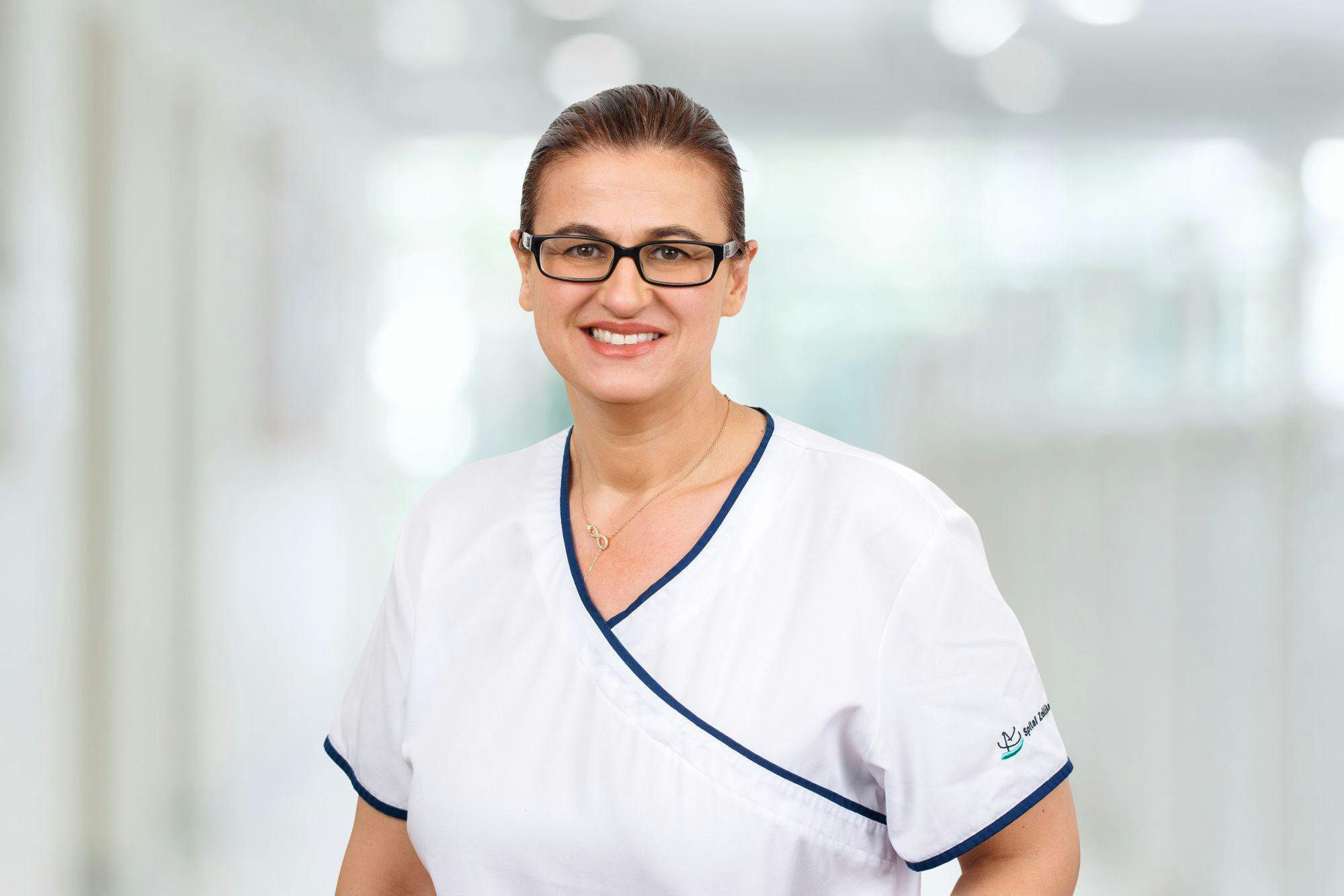 Smiling medical professional in white clothing with glasses.