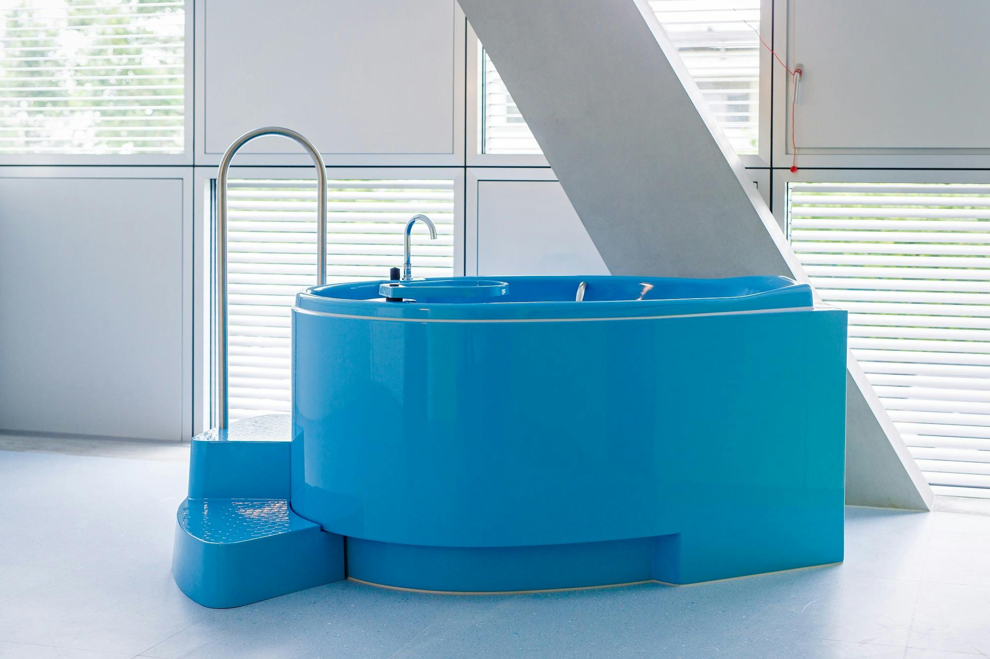 Modern blue round pool in a light-coloured interior with steps and stainless steel shower fitting.