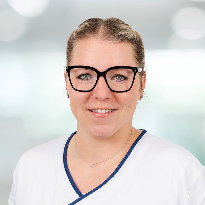 Porträt einer lächelnden Frau mit Brille im medizinischen Berufskleidung.