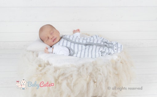 Schlafendes Neugeborenes in gestreiftem Strampelanzug auf weicher Decke.