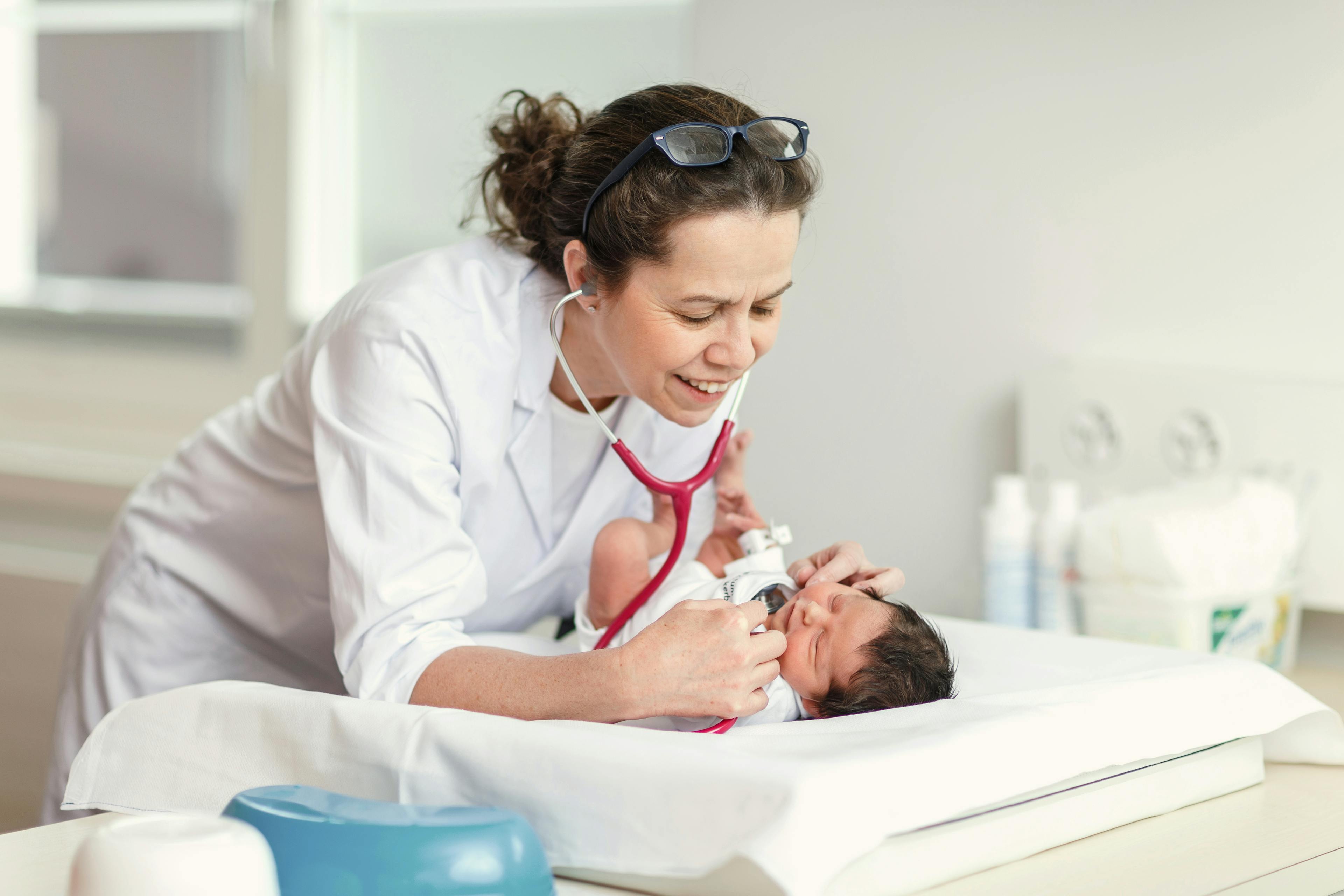 Eine Ärztin untersucht ein Neugeborenes mit einem Stethoskop in einer Klinik.