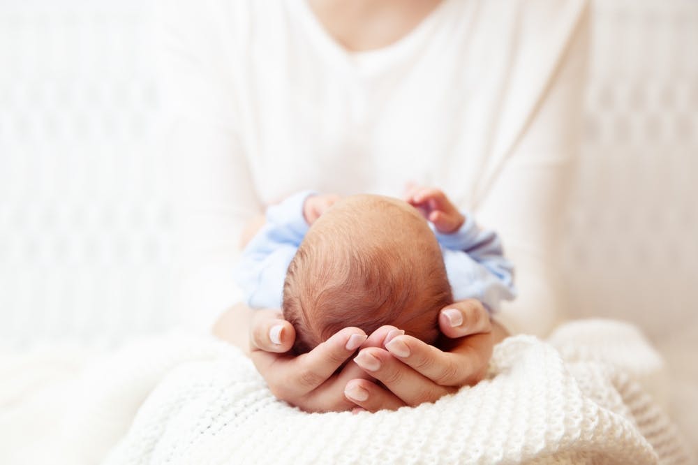 Newborn in hands, baby's head embraced with gentle touches.