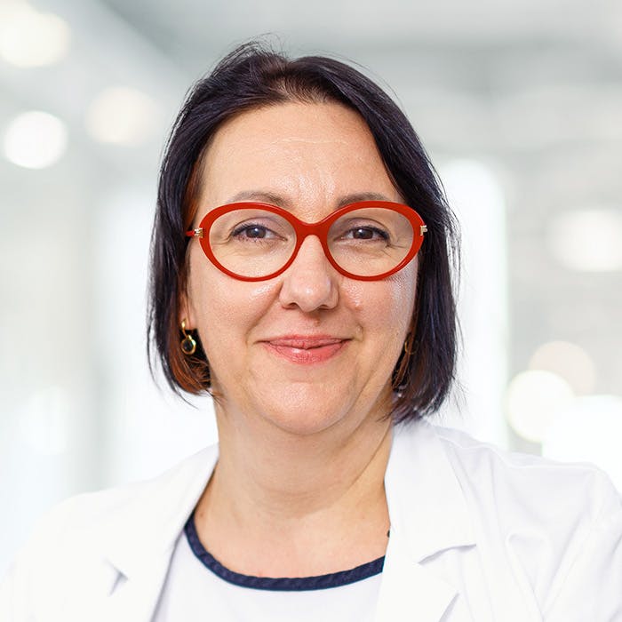 Woman with red glasses and a white lab coat smiles into the camera.