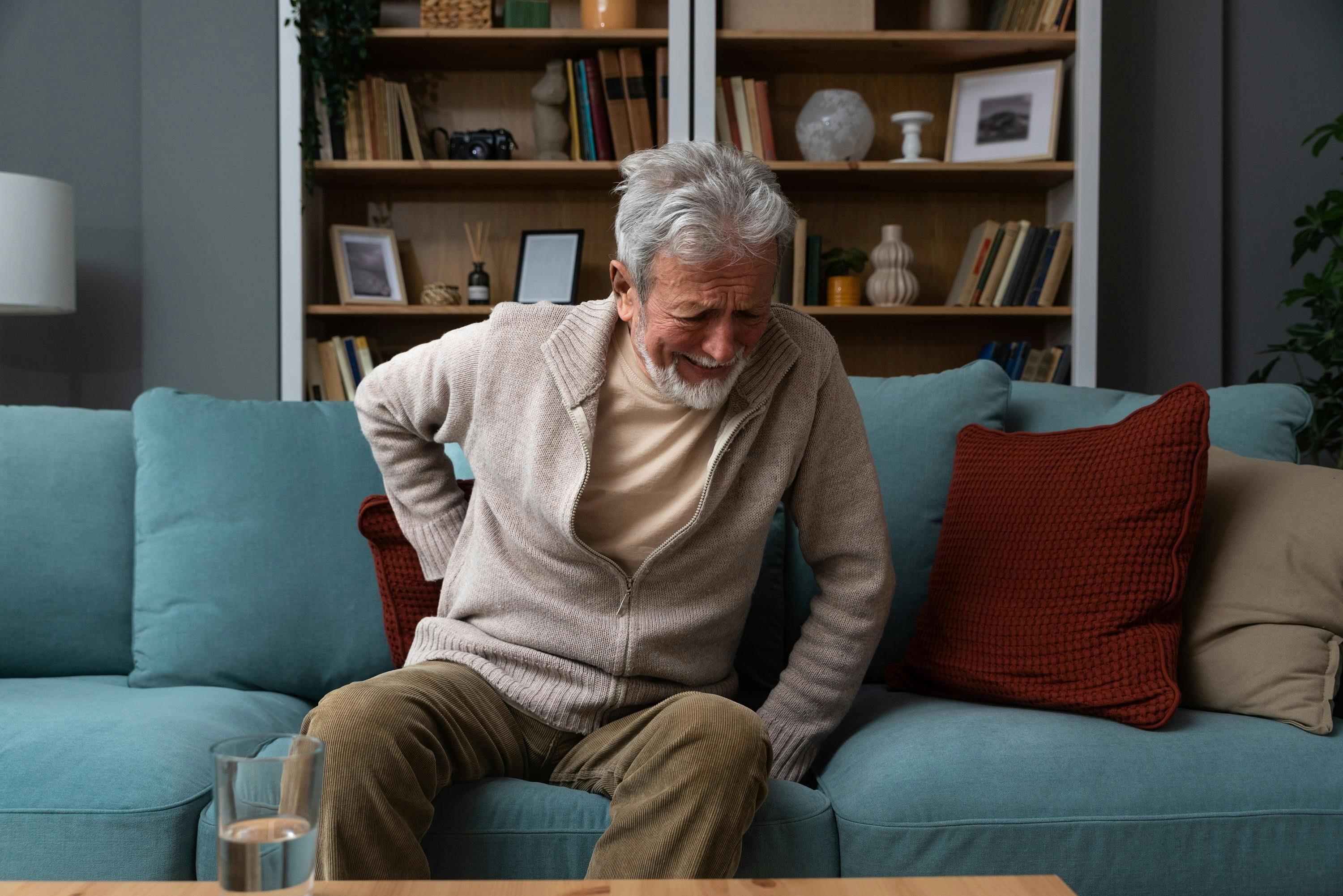Älterer Mann mit Schmerzen im Rücken sitzt auf einem Sofa im Wohnzimmer.