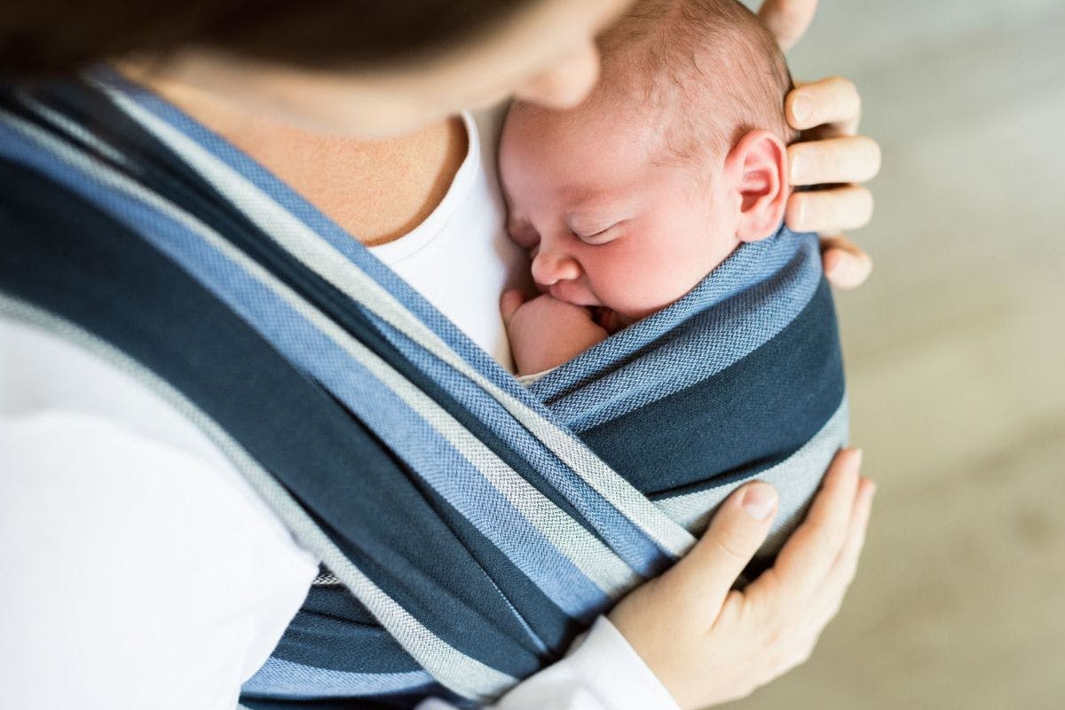 Mother holding sleeping newborn baby in a blue sling.