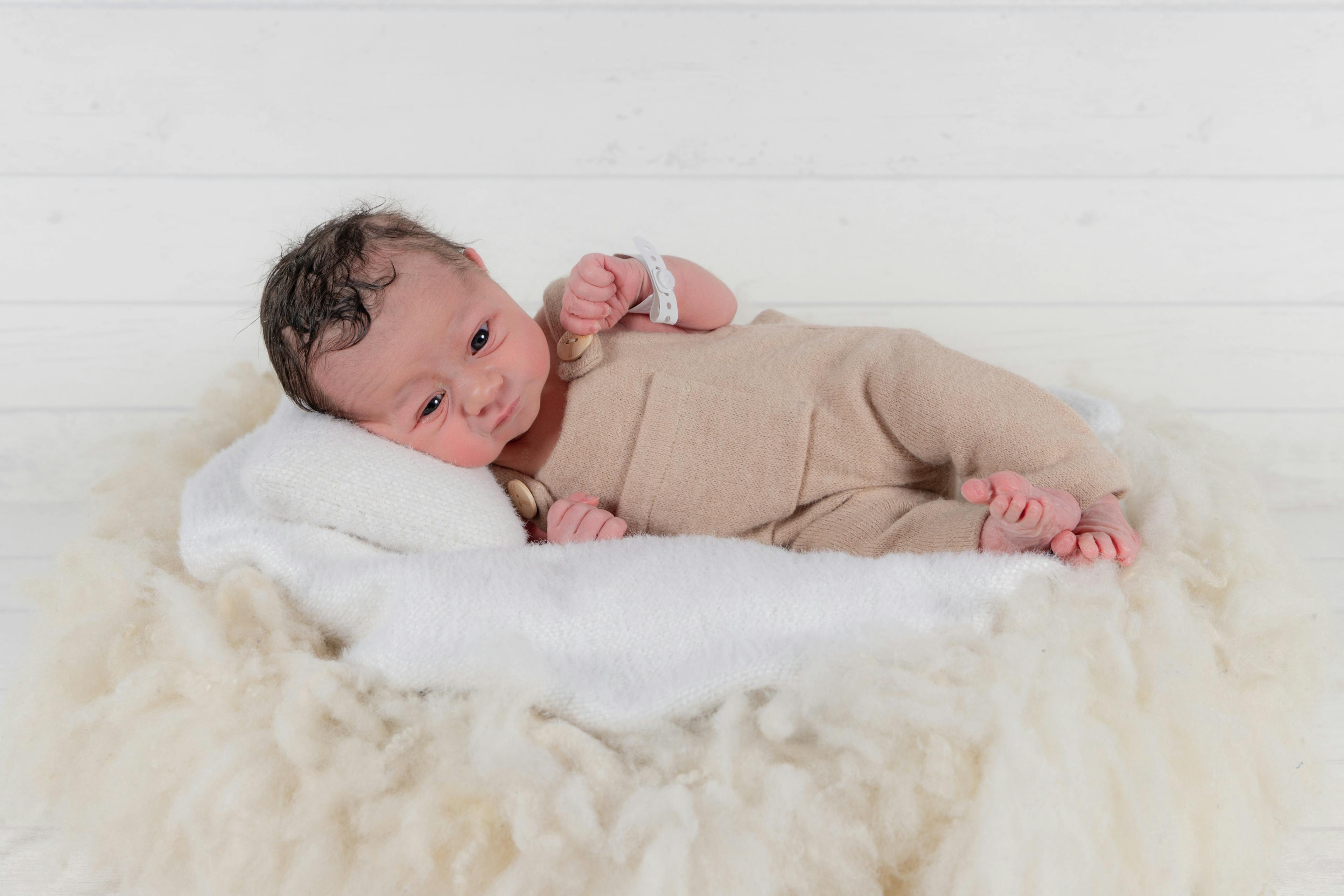 Newborn baby on a soft blanket with beige romper.